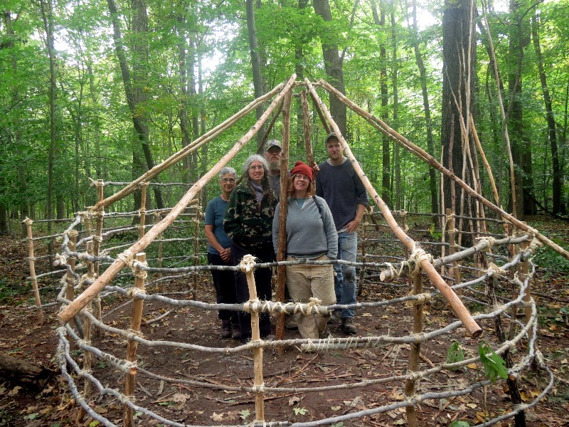 Primitive Bushcraft survival debris hut with campfire ring outside